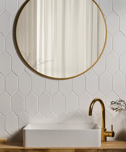 Bathroom with hexagonal white tiles, round gold mirror, and white sink with gold faucet.