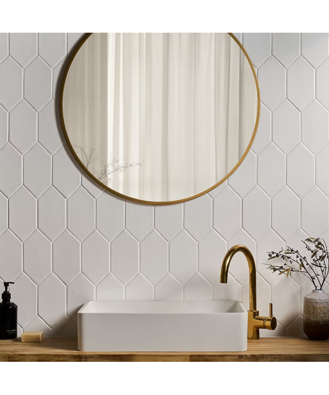 Bathroom with hexagonal white tiles, round gold mirror, and white sink with gold faucet.