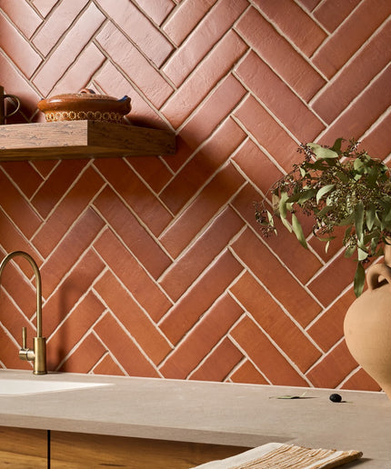 Terracotta wall tiles in a herringbone pattern behind a kitchen countertop and shelf