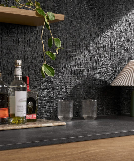 Bar setup with bottles, glasses, and a lamp against a textured black wall.