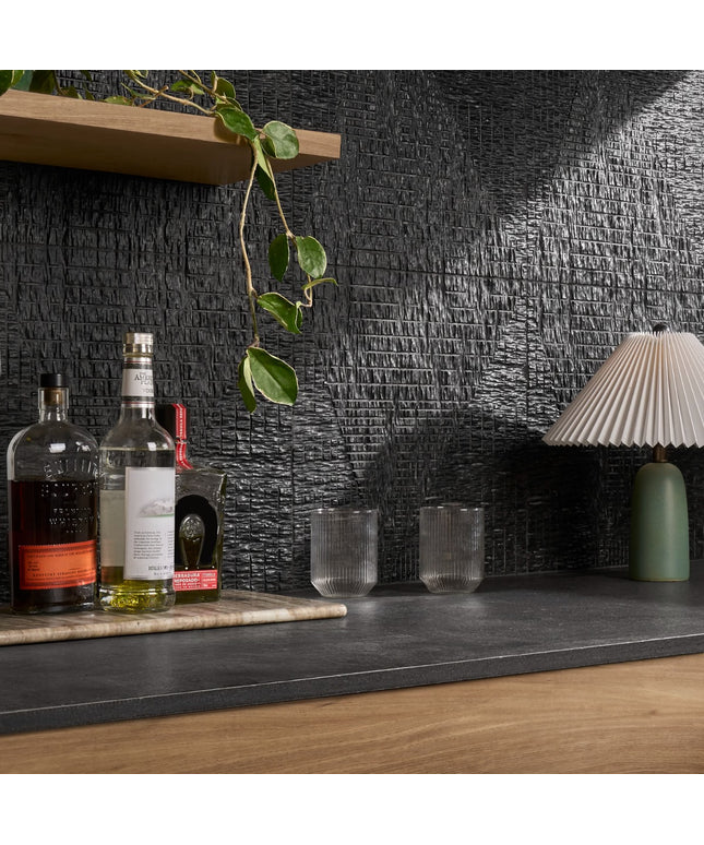 Bar setup with bottles, glasses, and a lamp against a textured black wall.