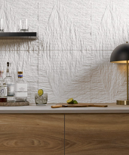 Modern kitchen counter with bottles, glasses, and a cutting board against a textured wall.
