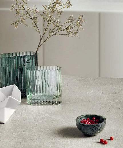 Decorative items including a green vase, glass, white bowl, and small black bowl with berries on a light surface.