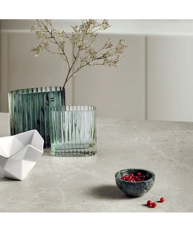 Decorative items including a green vase, glass, white bowl, and small black bowl with berries on a light surface.
