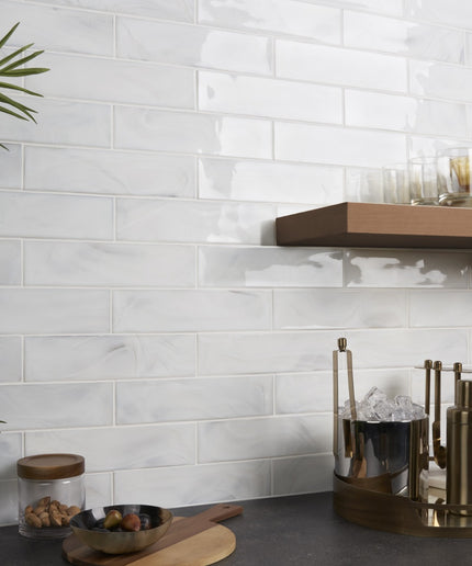 Kitchen counter with white tiled wall, wooden shelf, and decorative items.