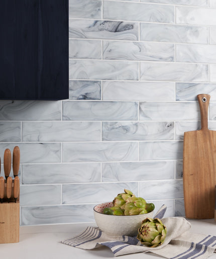 Kitchen scene with marble tile backsplash, cutting board, and fruit bowl.