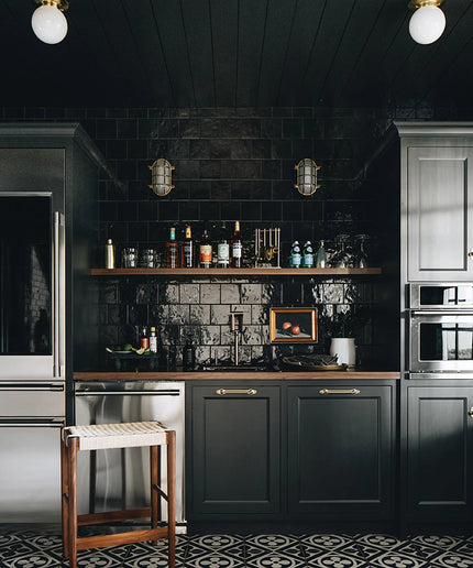 Modern kitchen with dark cabinets, black tiled walls, and stainless steel appliances.