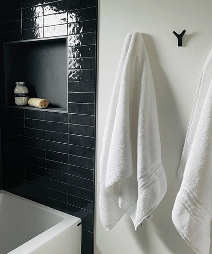 Bathroom with black tiled wall, white bathtub, and towels hanging on a hook.