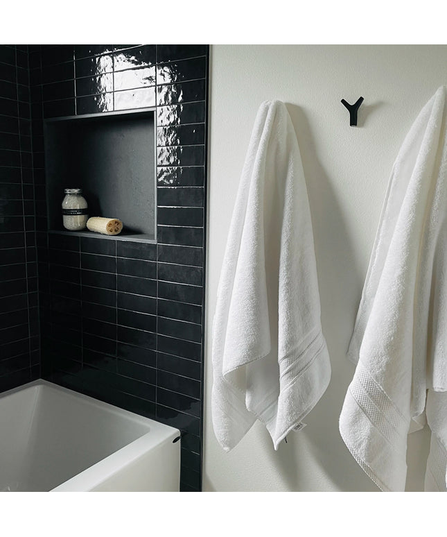 Bathroom with black tiled wall, white bathtub, and towels hanging on a hook.