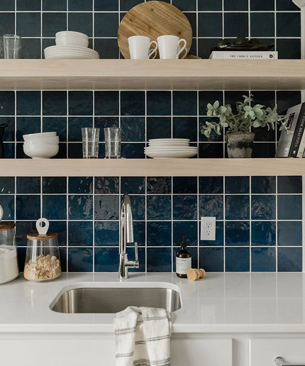 Modern kitchen with blue tiled wall, white countertops, and wooden shelves.