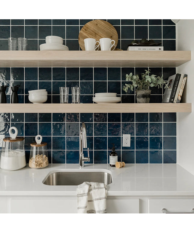 Modern kitchen with blue tiled wall, white countertops, and wooden shelves.