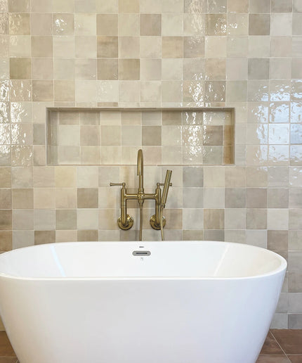 White freestanding bathtub with gold faucet against a tiled wall