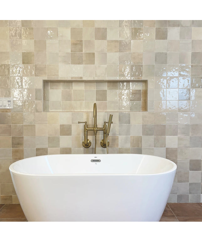White freestanding bathtub with gold faucet against a tiled wall