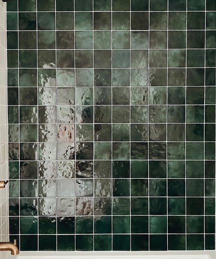 Green tiled wall with a shower head and handle in a bathroom setting