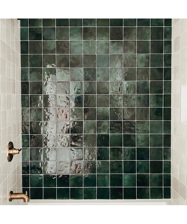 Green tiled wall with a shower head and handle in a bathroom setting