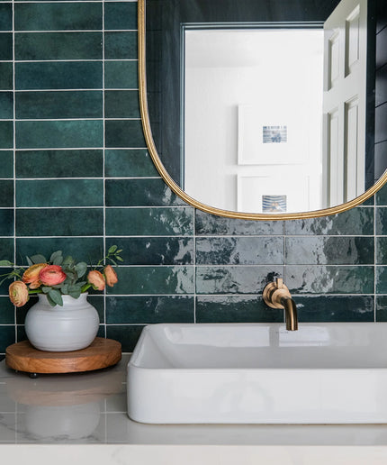 Bathroom with green tiles, white sink, and gold faucet.