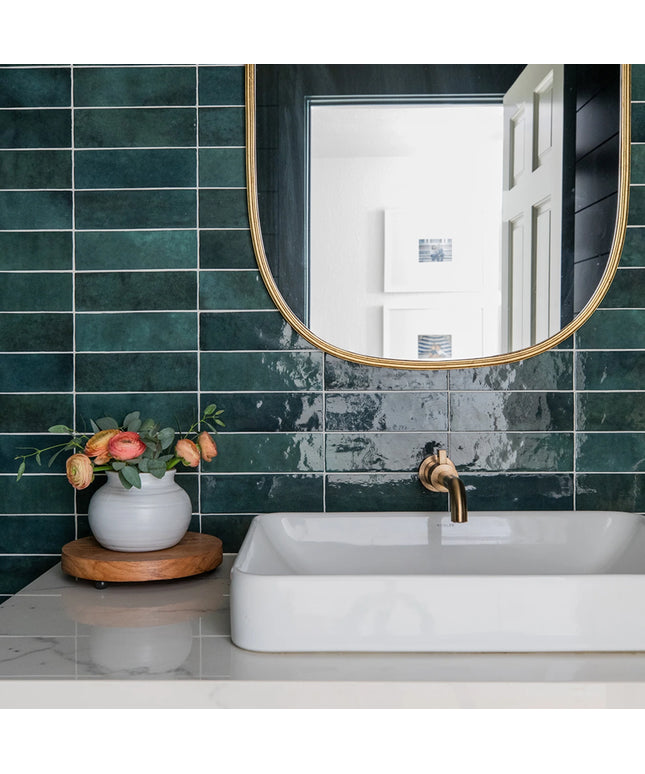 Bathroom with green tiles, white sink, and gold faucet.