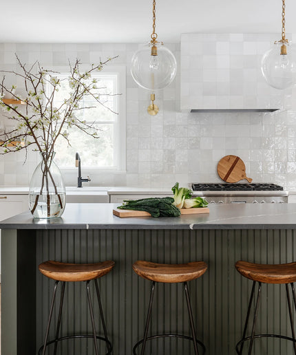 Modern kitchen with a island, stools, and a vase with branches.
