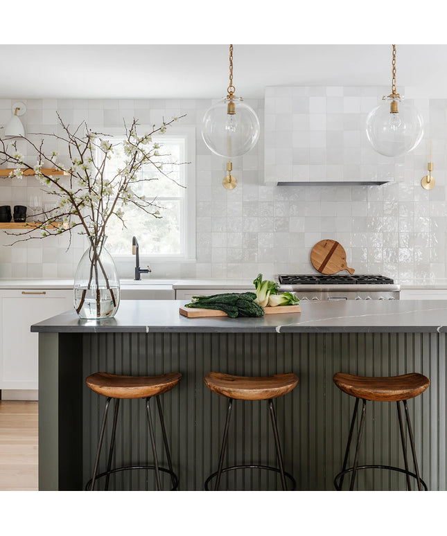 Modern kitchen with a island, stools, and a vase with branches.