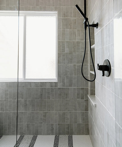 Modern shower setup with gray tiled walls and a black shower head.