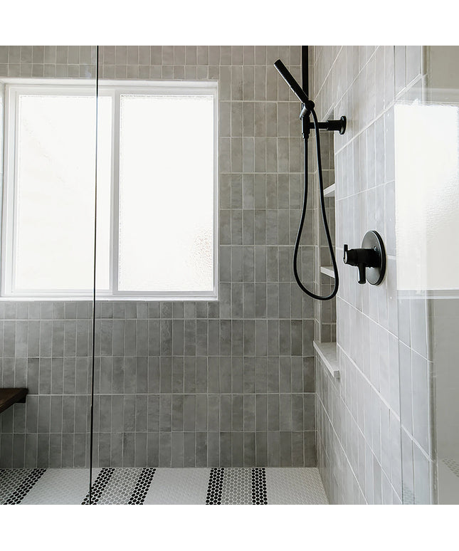 Modern shower setup with gray tiled walls and a black shower head.
