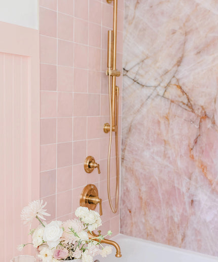 Bathroom with pink tiles, gold fixtures, and marble wall.