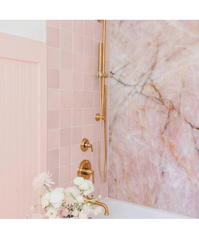 Bathroom with pink tiles, gold fixtures, and marble wall.