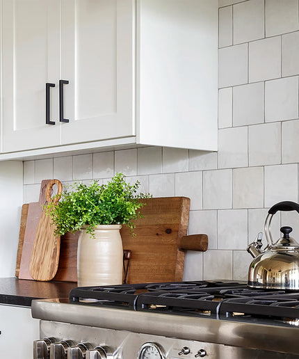 Kitchen with white cabinets, tiled wall, and stainless steel stove with a teakettle.