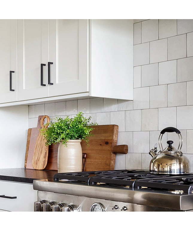Kitchen with white cabinets, tiled wall, and stainless steel stove with a teakettle.