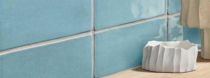 Close-up of blue tiled wall with a white decorative pot on a wooden floor.