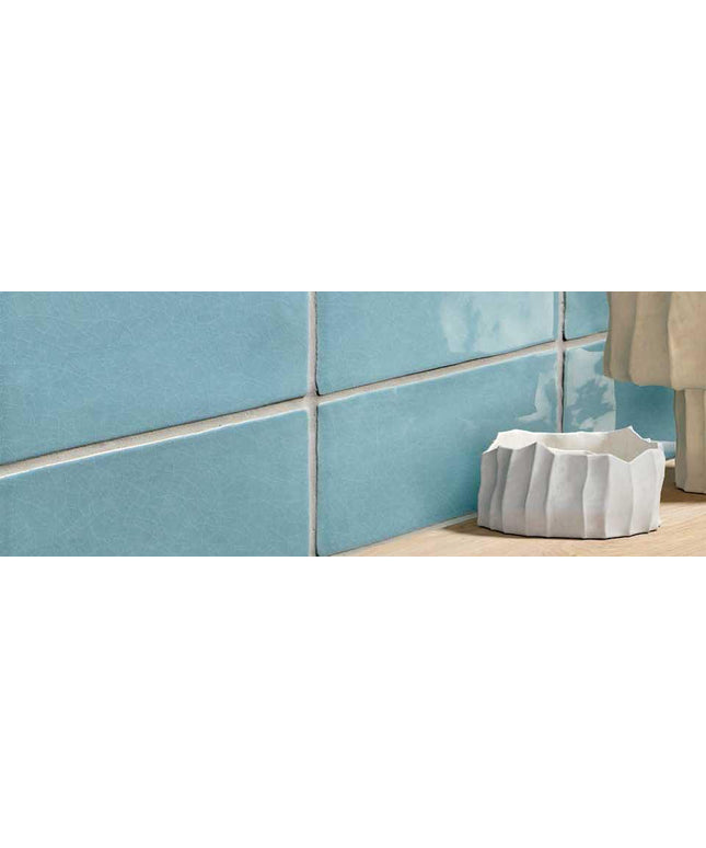 Close-up of blue tiled wall with a white decorative pot on a wooden floor.