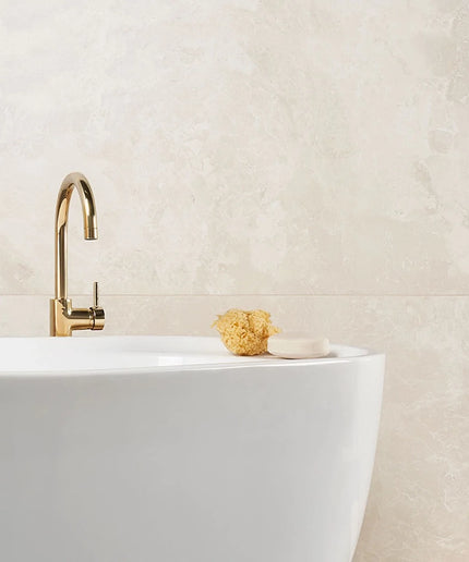Gold faucet on a white sink with a textured beige wall in the background