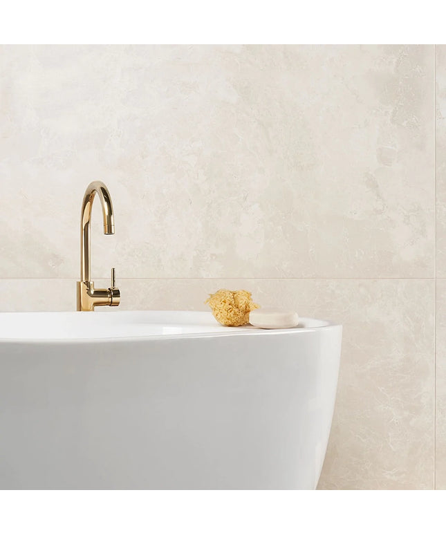 Gold faucet on a white sink with a textured beige wall in the background