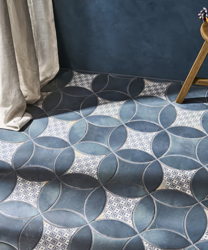 Patterned blue tiles on a floor with a curtain and small table in the background.