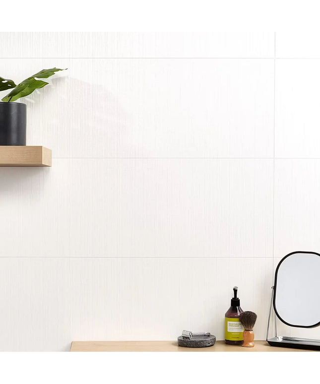 Small vanity setup with mirror, bottle, and plant on a white tiled wall background