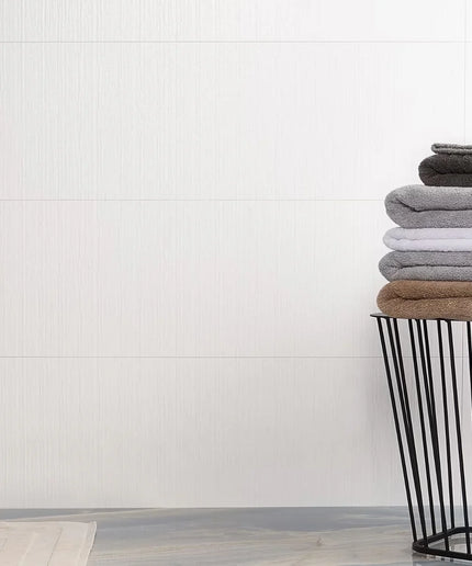 Stack of folded towels in a black wire basket against a white tiled wall.