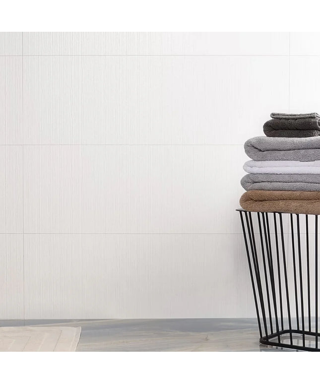 Stack of folded towels in a black wire basket against a white tiled wall.