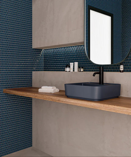 Bathroom with blue mosaic tiles, wooden shelf, and blue sink.