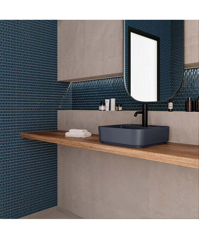 Bathroom with blue mosaic tiles, wooden shelf, and blue sink.