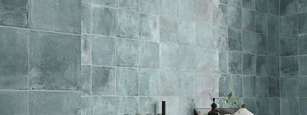 Teal tiled wall with a small plant and decorative item on a ledge.