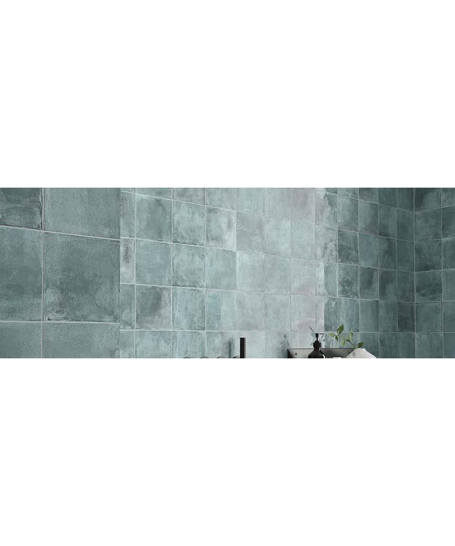 Teal tiled wall with a small plant and decorative item on a ledge.
