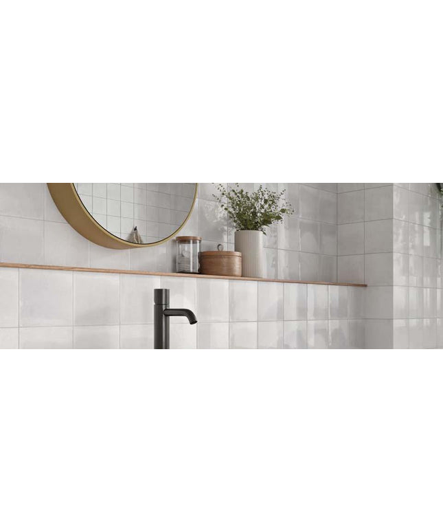 Bathroom with white tiled walls, wooden shelf, and decorative items.