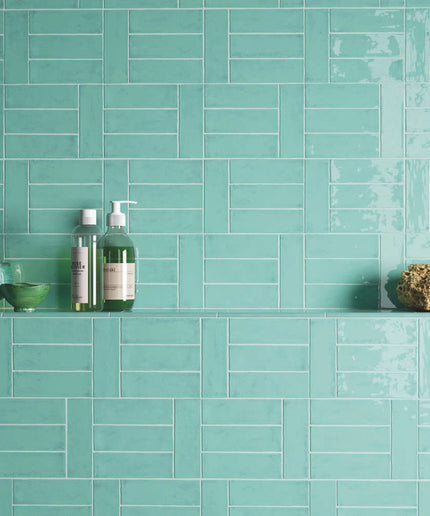 Aqua marine bathroom wall tiles with shelf, bath products, and green decor bowls.