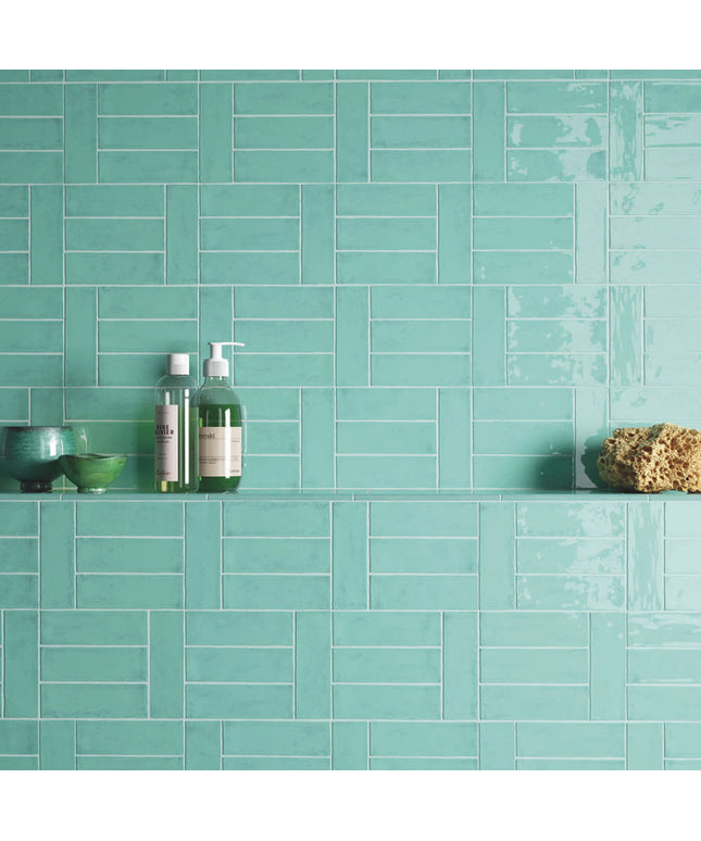 Aqua marine bathroom wall tiles with shelf, bath products, and green decor bowls.