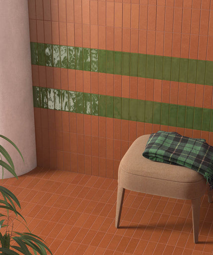 Terracotta wall and floor tiles with green accent tiles in a modern room with a chair and plant