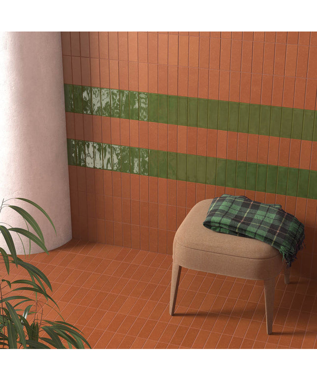Terracotta wall and floor tiles with green accent tiles in a modern room with a chair and plant