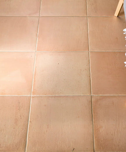 Beige tiles on a floor with a small table and chair in the corner.