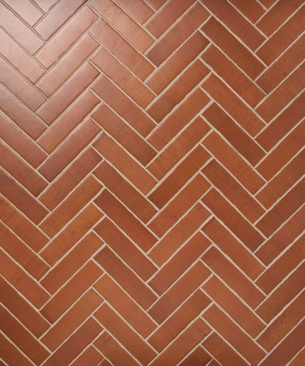 Herringbone pattern terracotta floor tiles with warm reddish-brown color and white grout lines