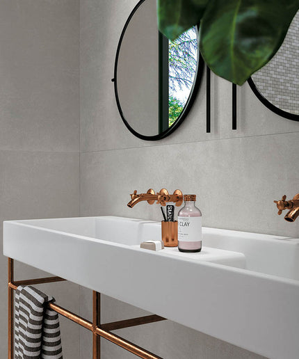 Modern bathroom with large neutral wall tiles, white sink, copper faucets, round mirrors