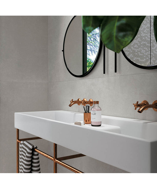 Modern bathroom with large neutral wall tiles, white sink, copper faucets, round mirrors